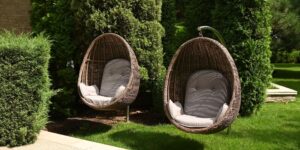View of a green lawn and wicker rattan chairs-shells for relaxing, hotel, hanging bench seat chair in basket design on the green grass field, Rattan chair on the lawn, Shallow depth of field, Needles